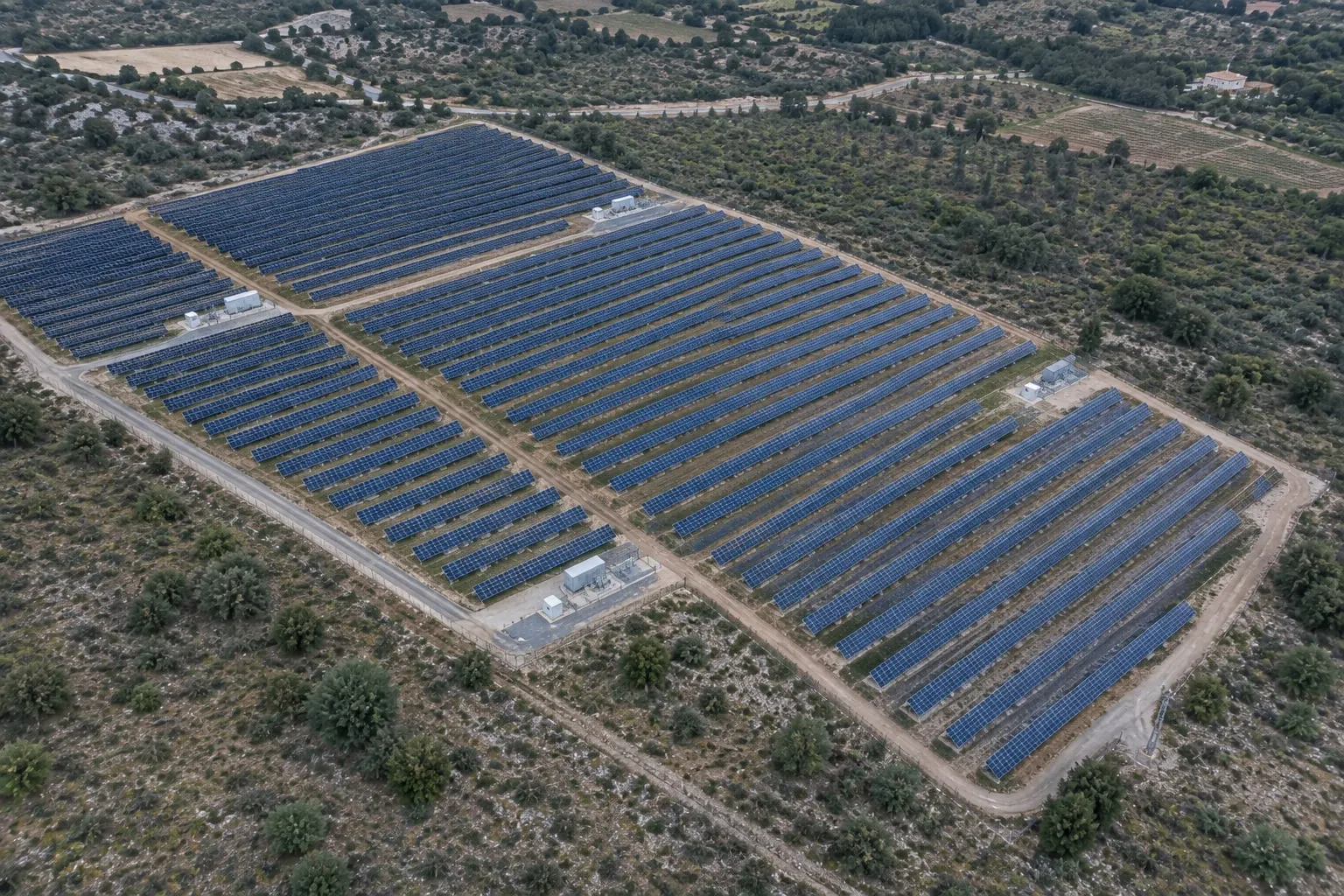 Centrale solaire au sol vue du ciel, rangées de panneaux au milieu de la garrigue