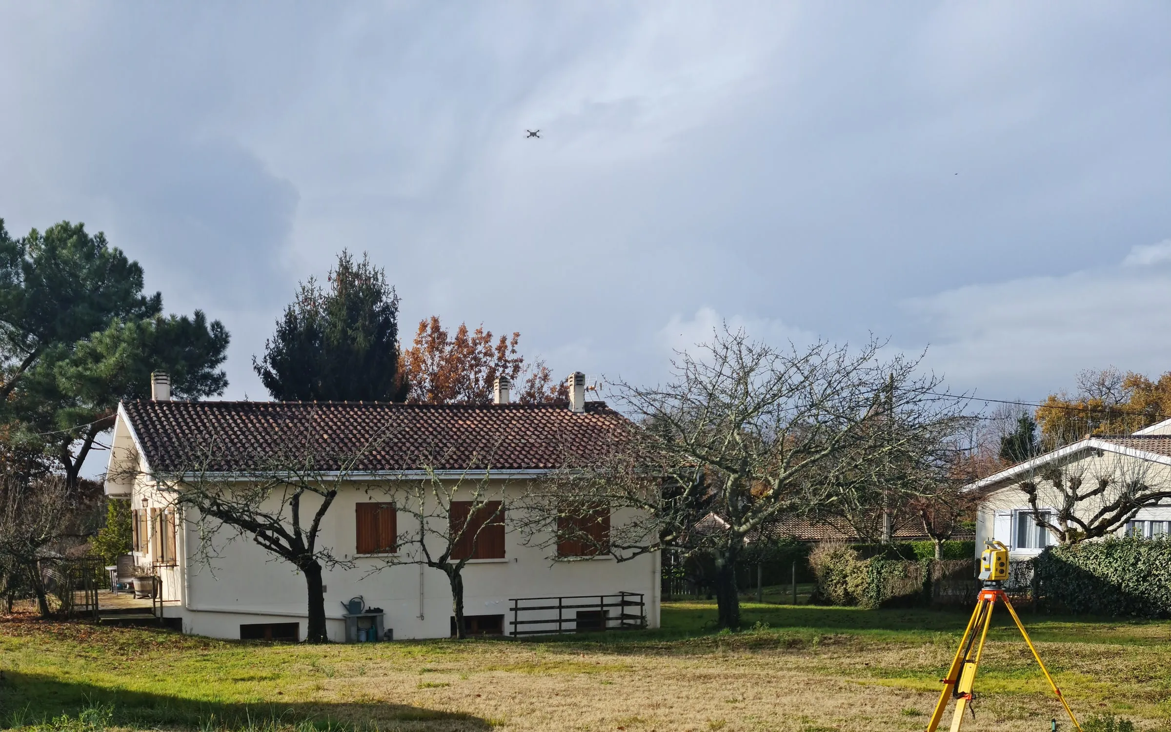 Drone en vol au-dessus d'une maison à relever, station totale installée sur le terrain